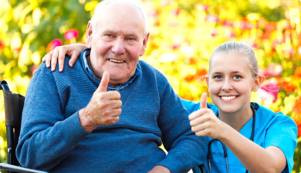an elderly man with her caregiver doing thumbs up while smiling