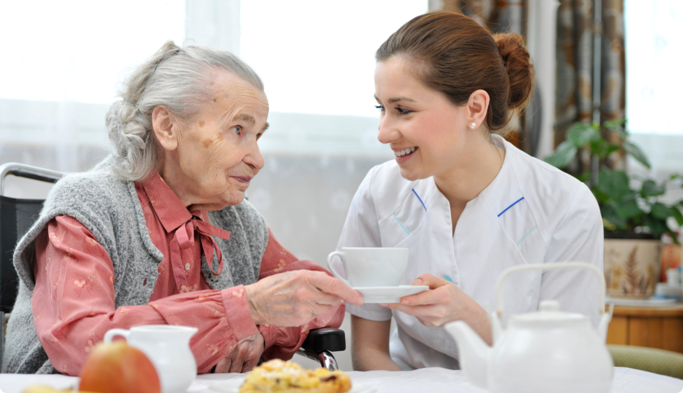 caregiver serving coffee to an elderly woman